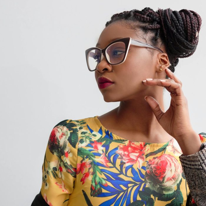 Elegant portrait featuring a woman in glasses with braided hairstyle and floral top.
